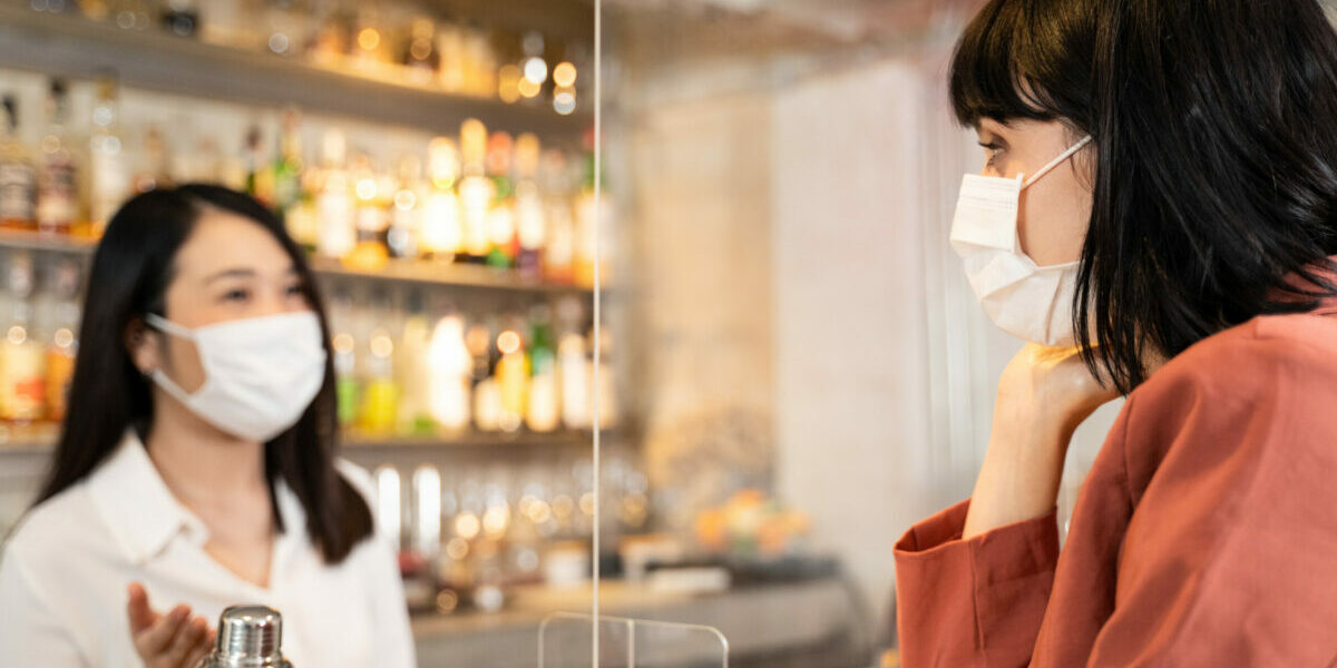Bartender serving patron behind a plexiglass divider